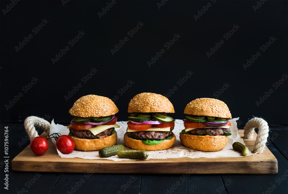Fresh beef burgers with cheese, vegetables, pickles and spicy tomato sauce on paper over rustic wood