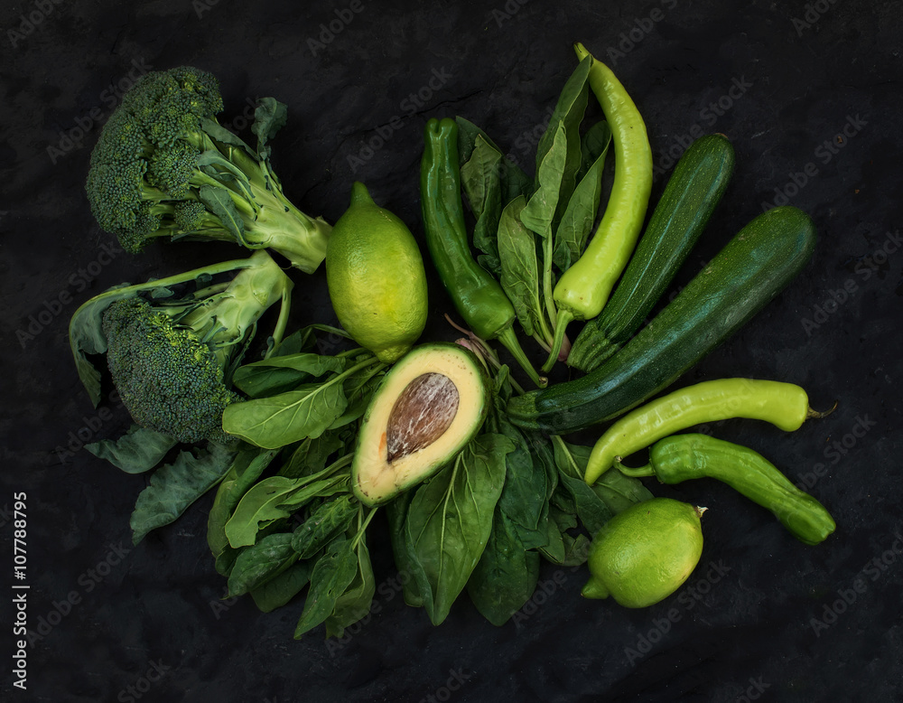 生绿色蔬菜套装。西兰花、鳄梨、胡椒、菠菜、祖奇尼和青柠在深色石头背上。