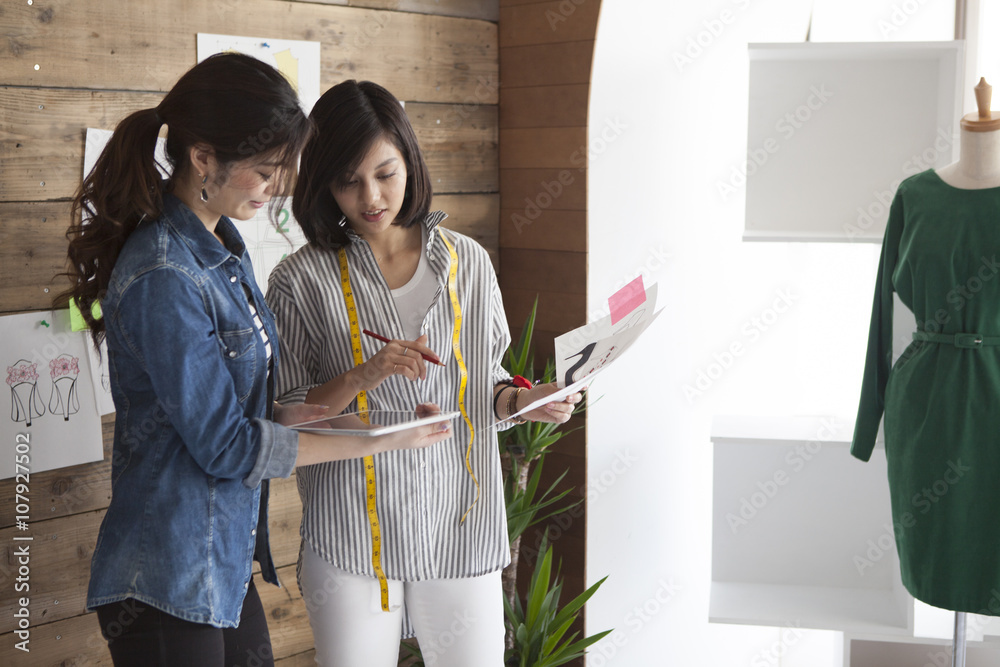 两位年轻女性一边看着平板电脑，一边想着设计的鞋子