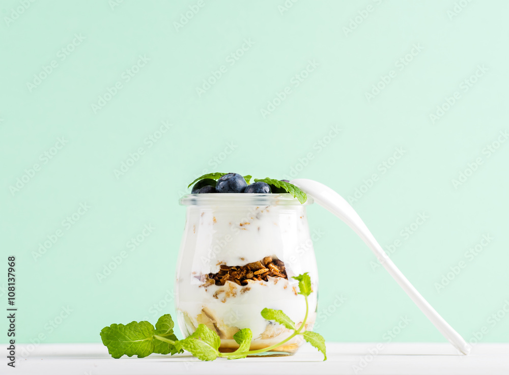 酸奶燕麦格兰诺拉麦片配果酱、蓝莓和绿叶，装在薄荷背景的玻璃罐里