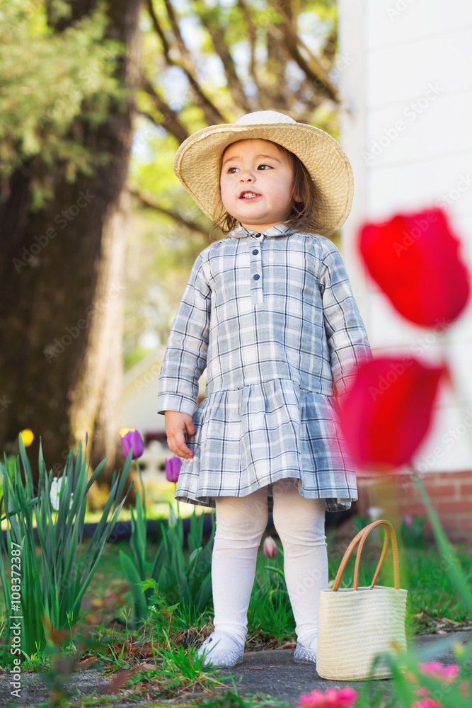 戴着帽子的蹒跚学步的女孩探索她的花园