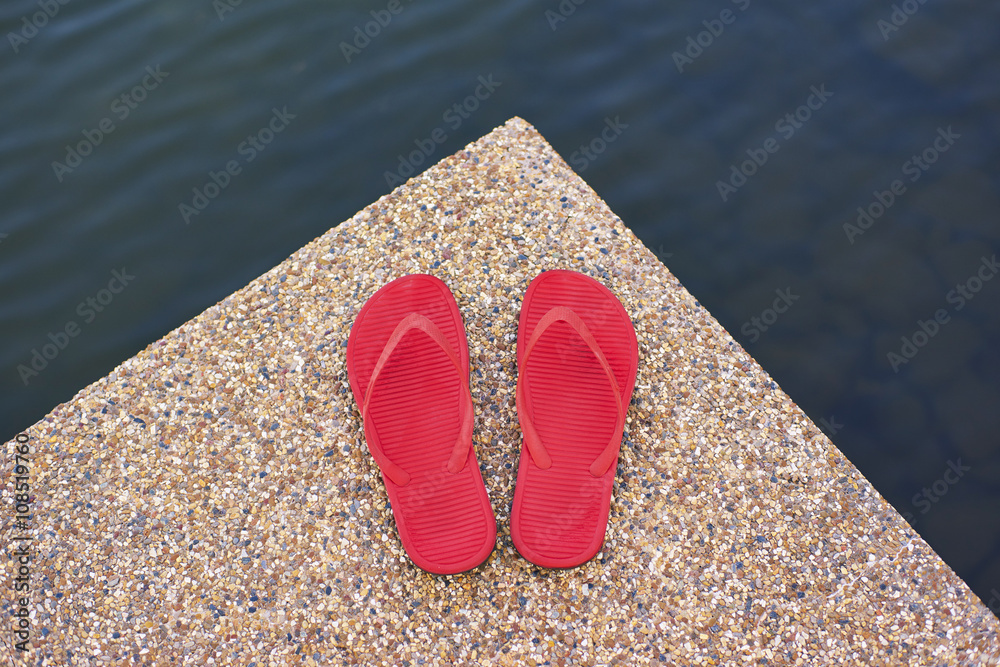 一双红色舒适拖鞋放置在石头地板的湖边