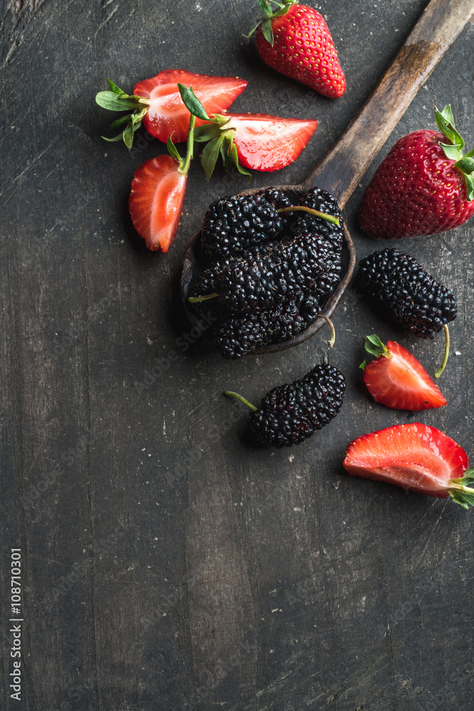 Berries on dark wooden background. Fresh strawberries and mulberries in rustic cooking spoon 