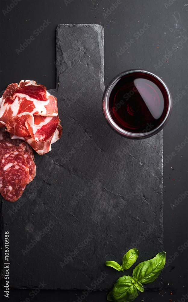 一杯红酒、肉类开胃菜和罗勒，黑色石板石板，深色背景