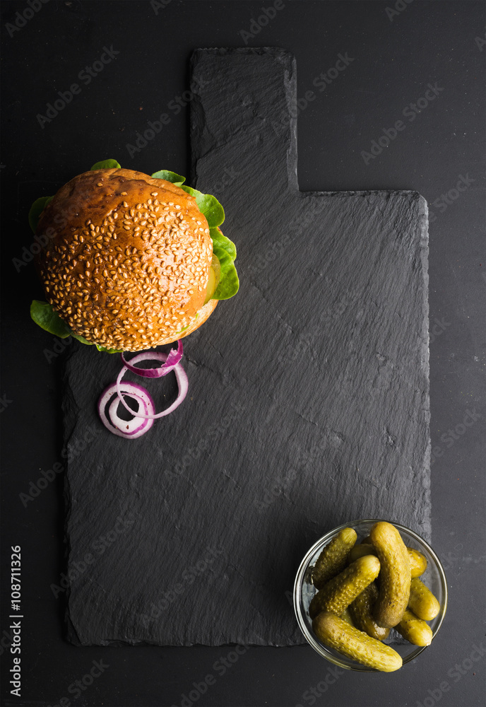 深色石板石板上的新鲜自制汉堡，黑色背景上的泡菜和洋葱片。