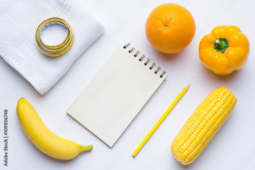 Yellow items. Fitness concept with banana, coin, orange,  measuring tape on white background. View f