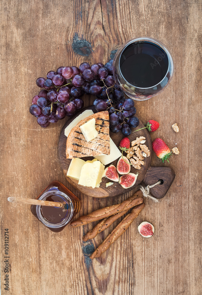 Glass of red wine, cheese board, grapes,fig, strawberries, honey and bread sticks  on rustic wooden 