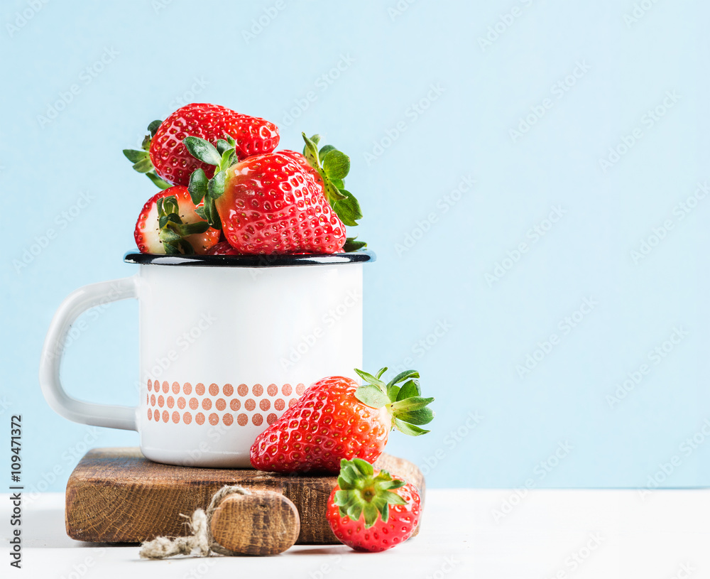 Fresh ripe red strawberries in country style enamel mug on rustic wooden board, pastel light blue ba
