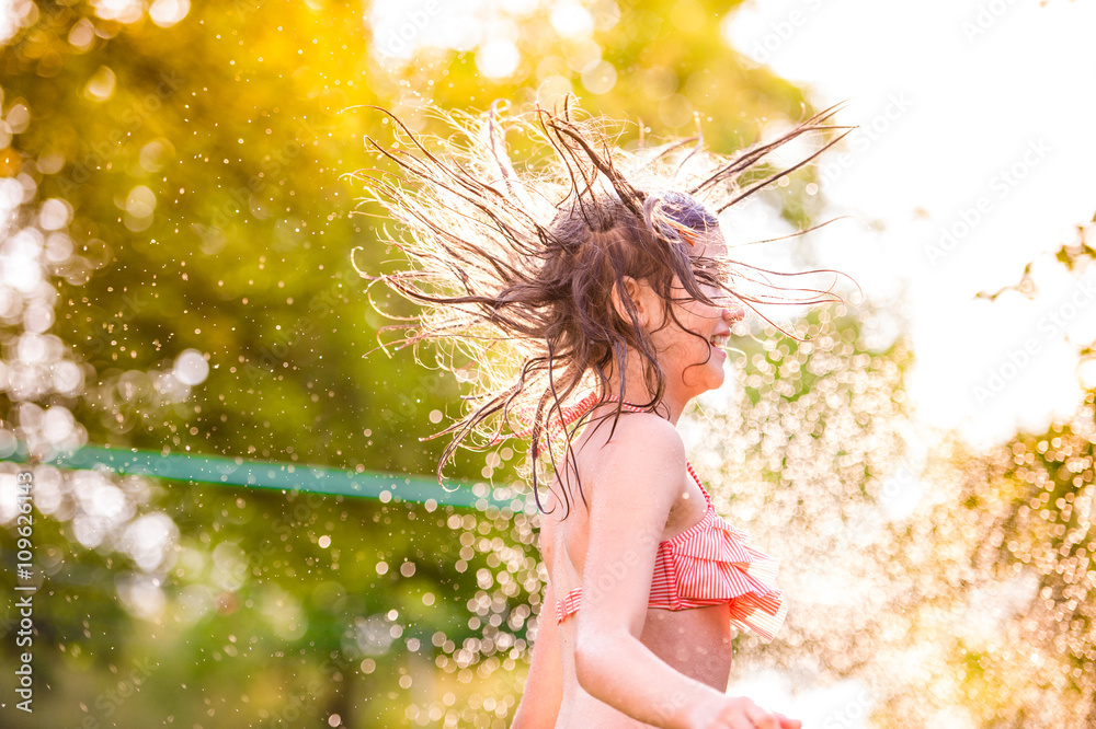 穿着比基尼的女孩在洒水喷头前跳舞，夏日花园