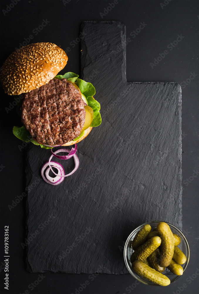 深色石板石板上的新鲜自制汉堡，黑色背景上的泡菜和洋葱片。