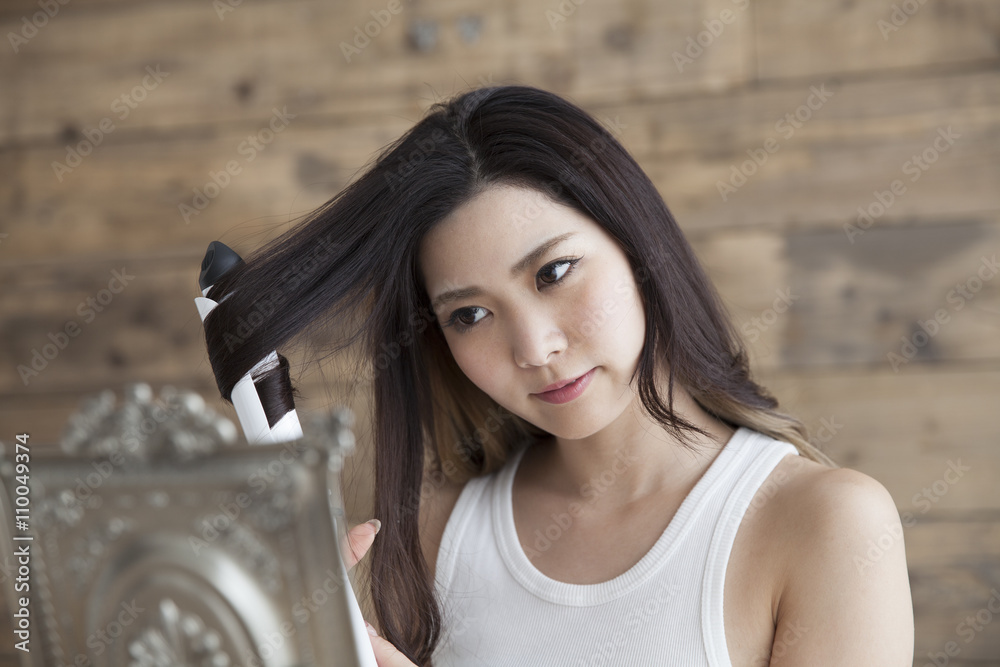 年轻女性在照镜子时被头发熨斗包裹在头发上