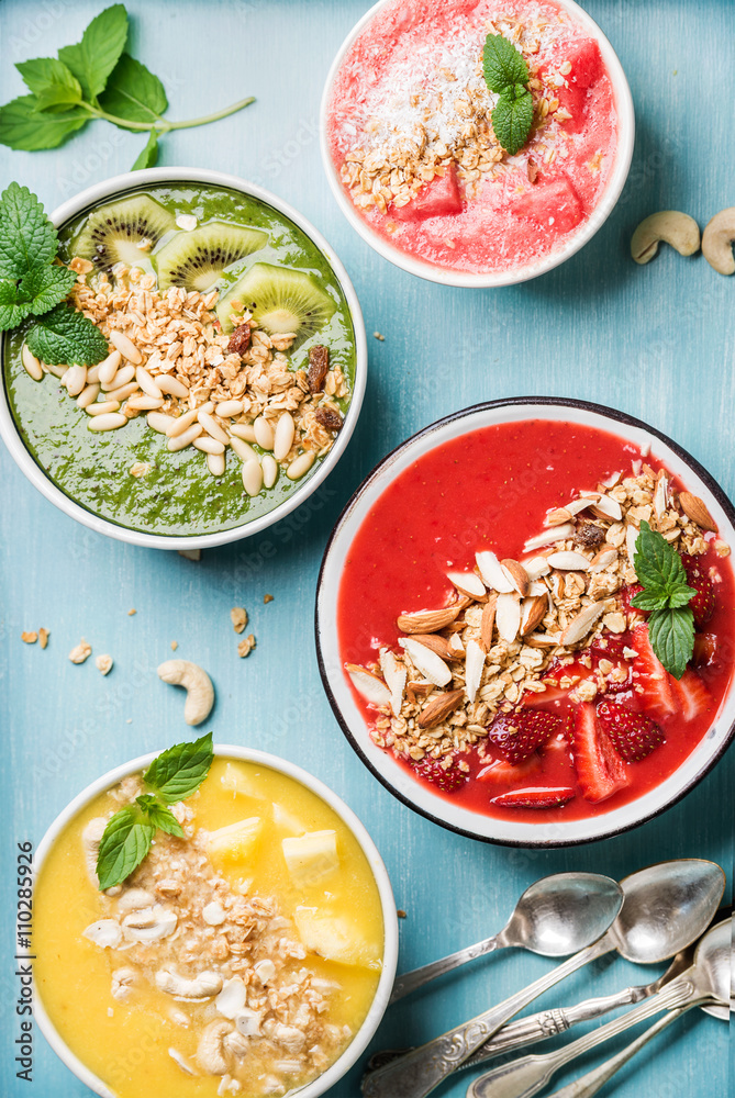 健康的夏季早餐概念。绿松石蓝色背景的彩色水果奶昔碗