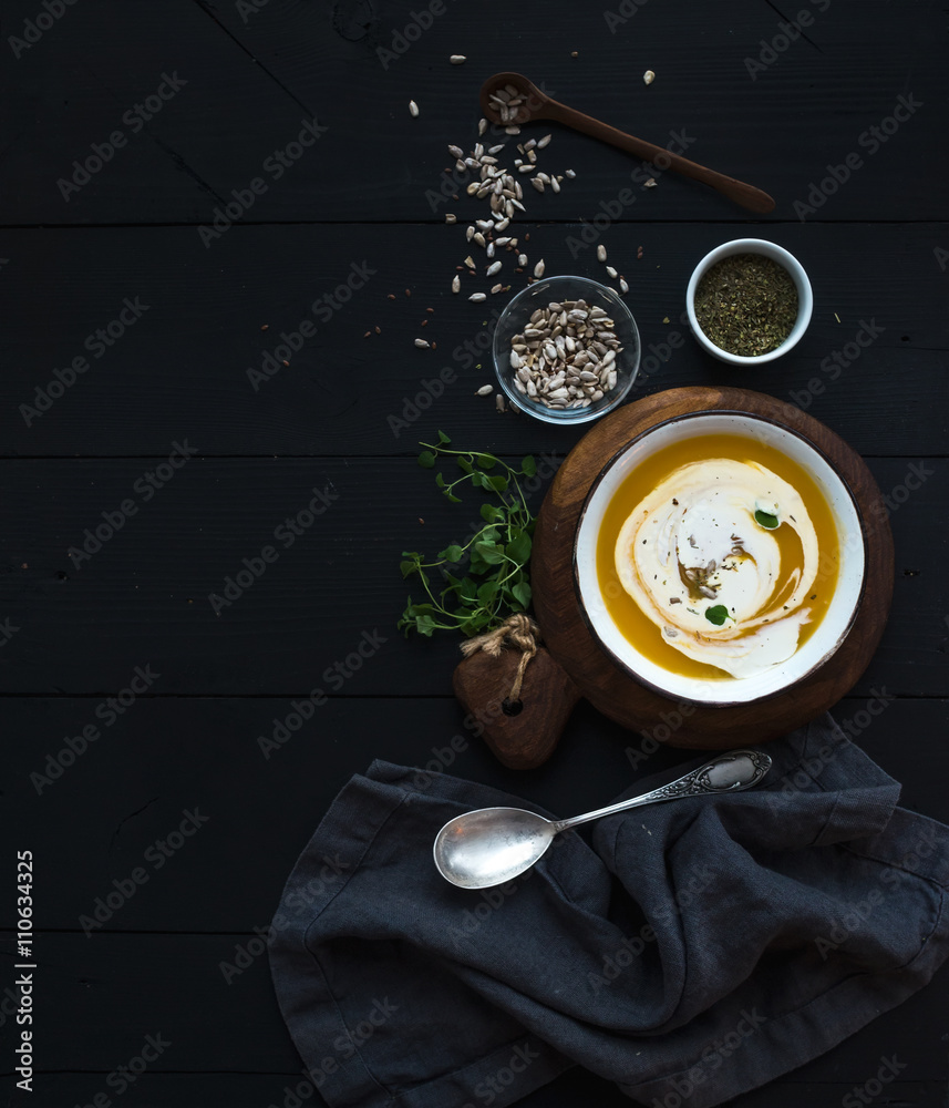 南瓜汤，奶油、种子和香料，装在乡村金属碗中，黑色背景。俯视图。