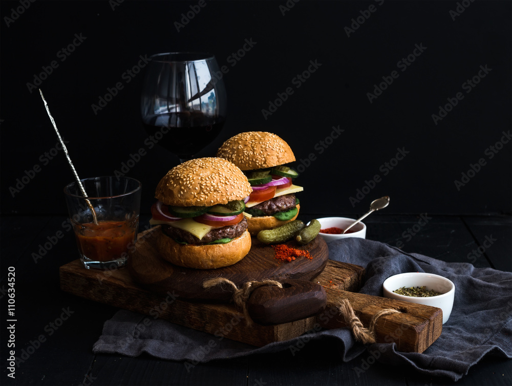在乡村木板上的新鲜牛肉汉堡，配一杯葡萄酒和番茄酱，黑色背景。