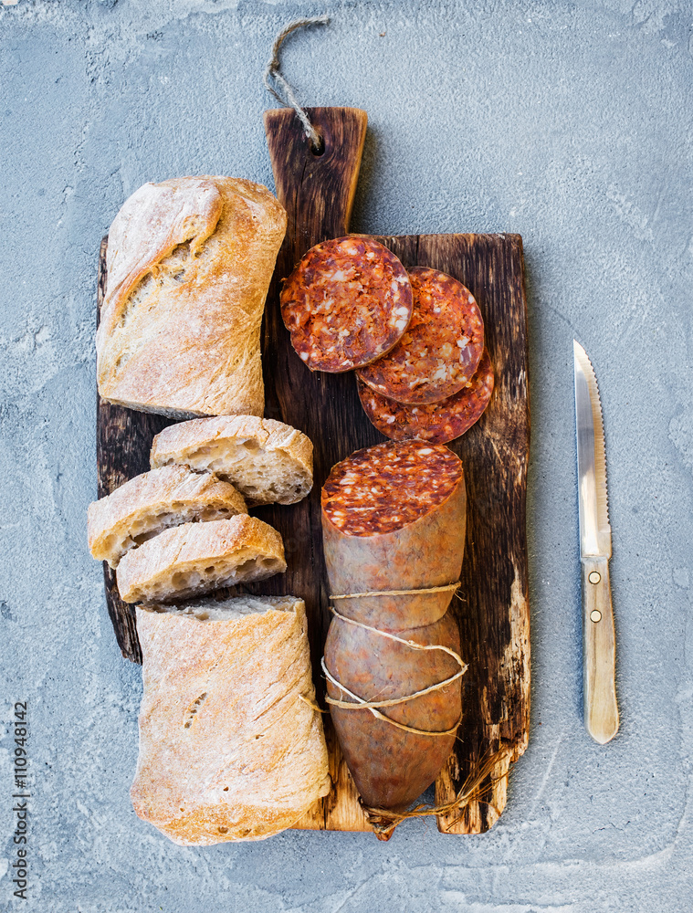 葡萄酒小吃套装。匈牙利曼加利卡猪肉香肠和乡村面包放在深色木板上。