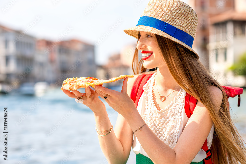 年轻的女性旅行者在威尼斯的运河背景下吃传统的意大利披萨片