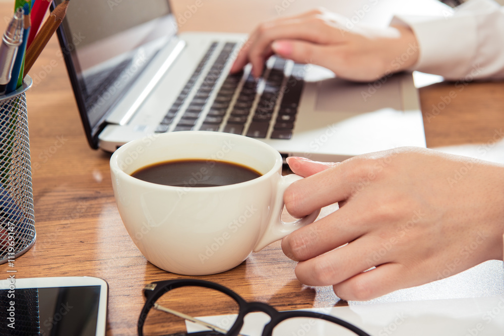 女商人在办公桌上用笔记本电脑喝咖啡