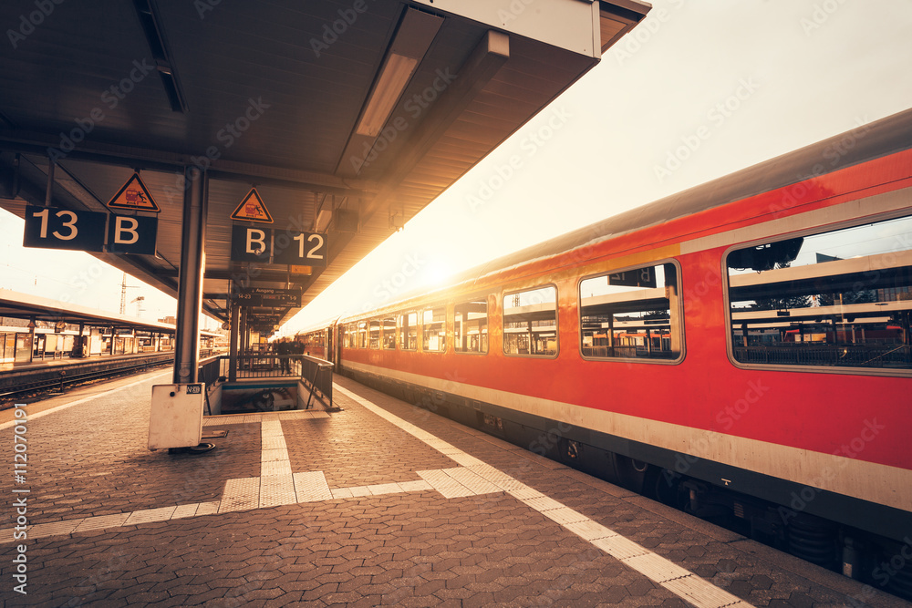 Beautiful railway station with modern red commuter train at colorful sunset in Nuremberg, Germany. R