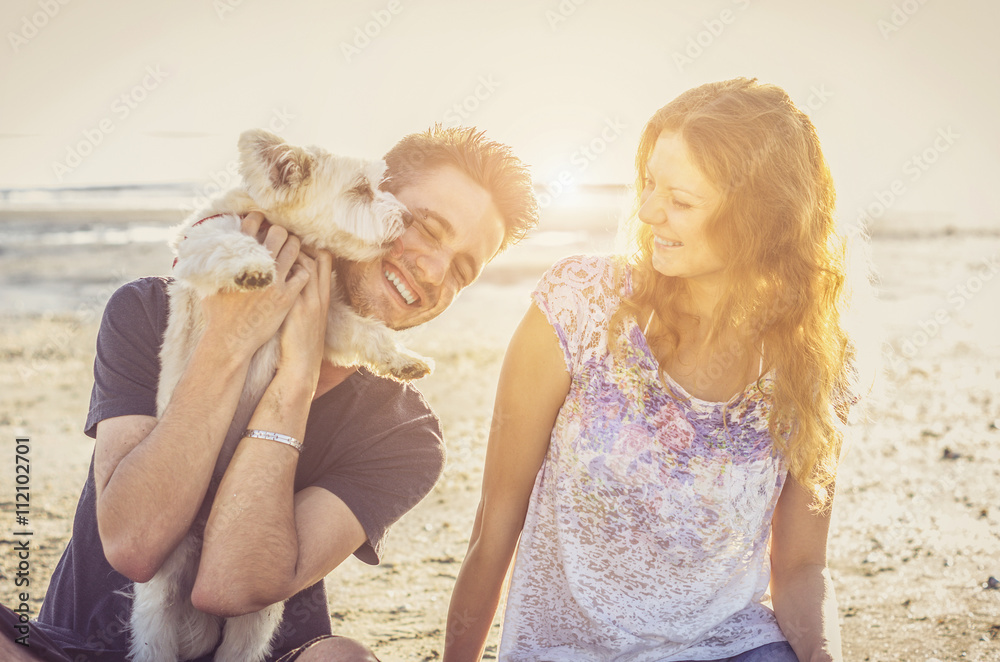 一对恩爱的情侣在海滩上和狗玩耍