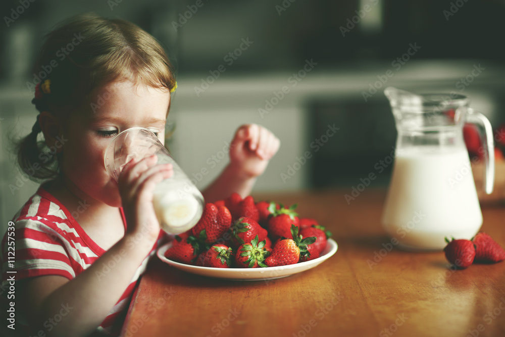 快乐的小女孩在夏天喝牛奶吃草莓