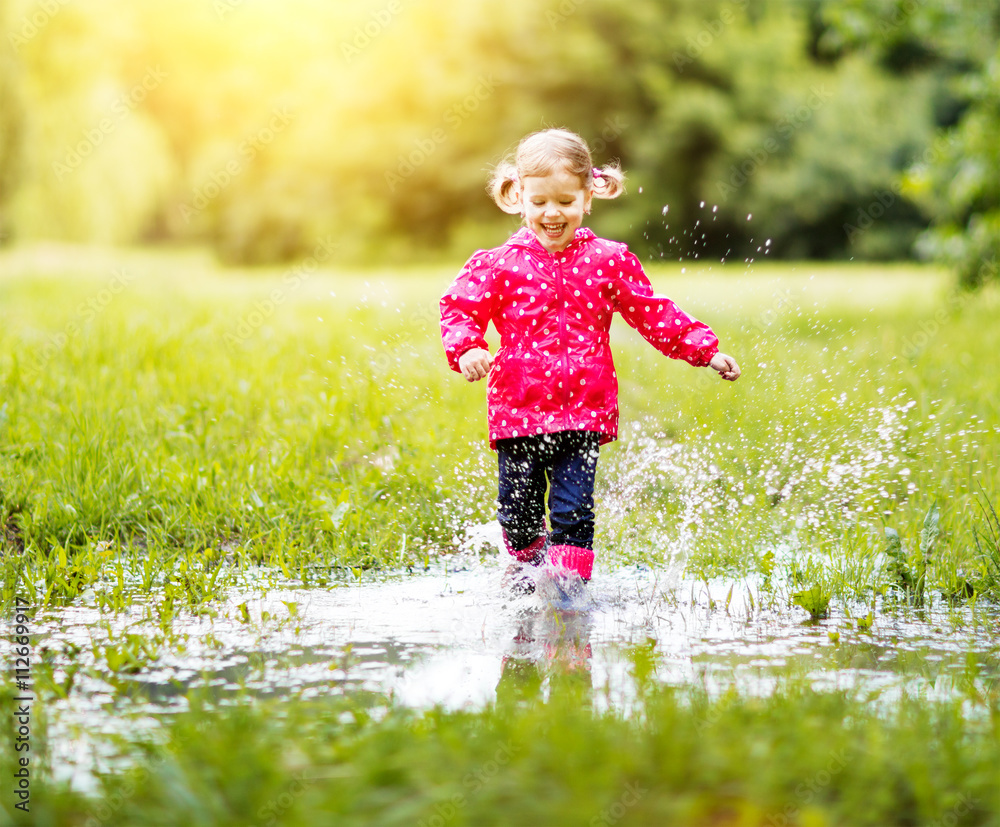 happy child girl running and jumping in puddles after rain