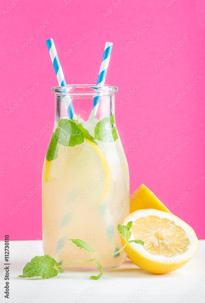 一瓶自制柠檬水，配薄荷、冰块、柠檬、纸吸管和亮紫色背景