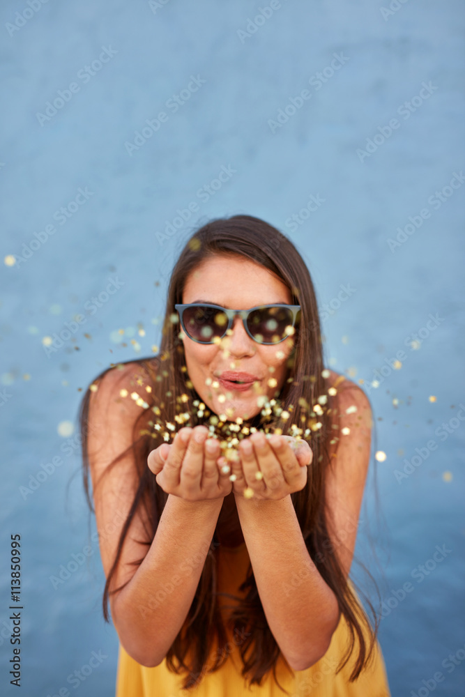 Happy young woman blowing confetti in the air