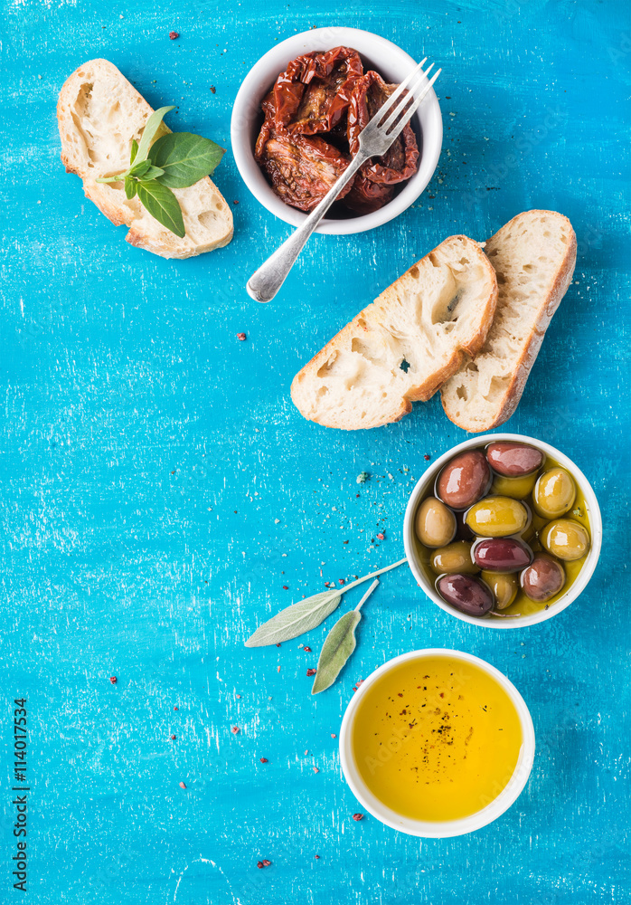 Mediterranean snacks set. Olives, oil, sun-dried tomatoes, herbs and sliced ciabatta bread on over b