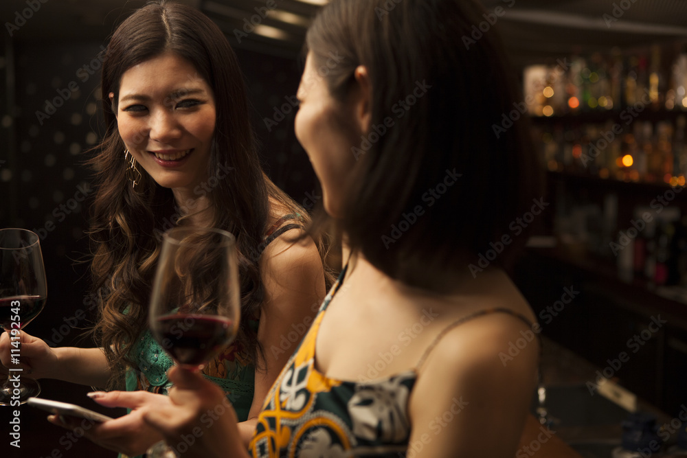 Young women looking at a smart phone with a glass of wine at the bar