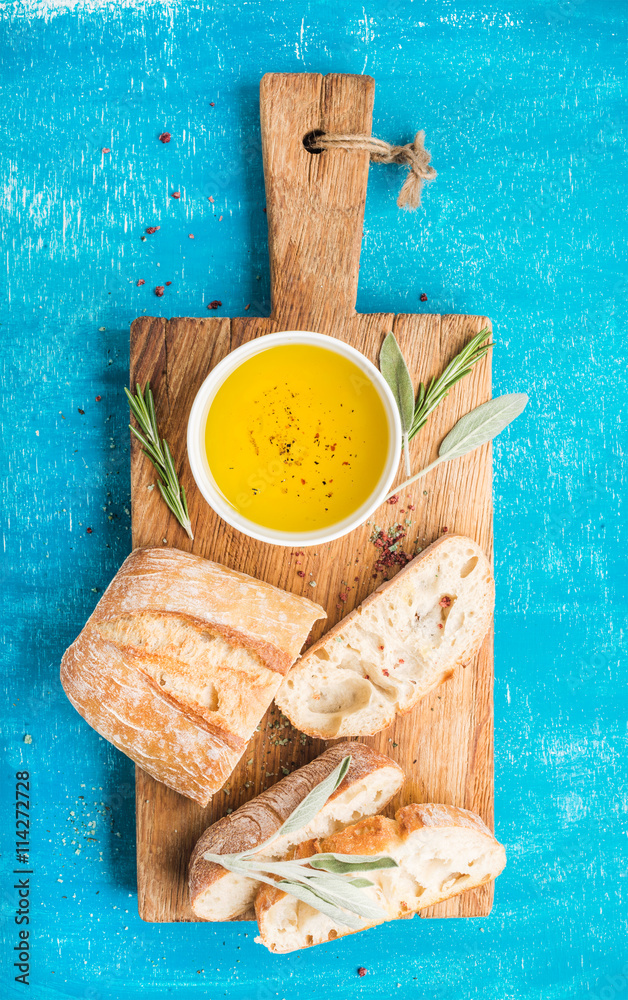 地中海小吃套装。乡村木板上的橄榄油、香草和切好的ciabatta面包