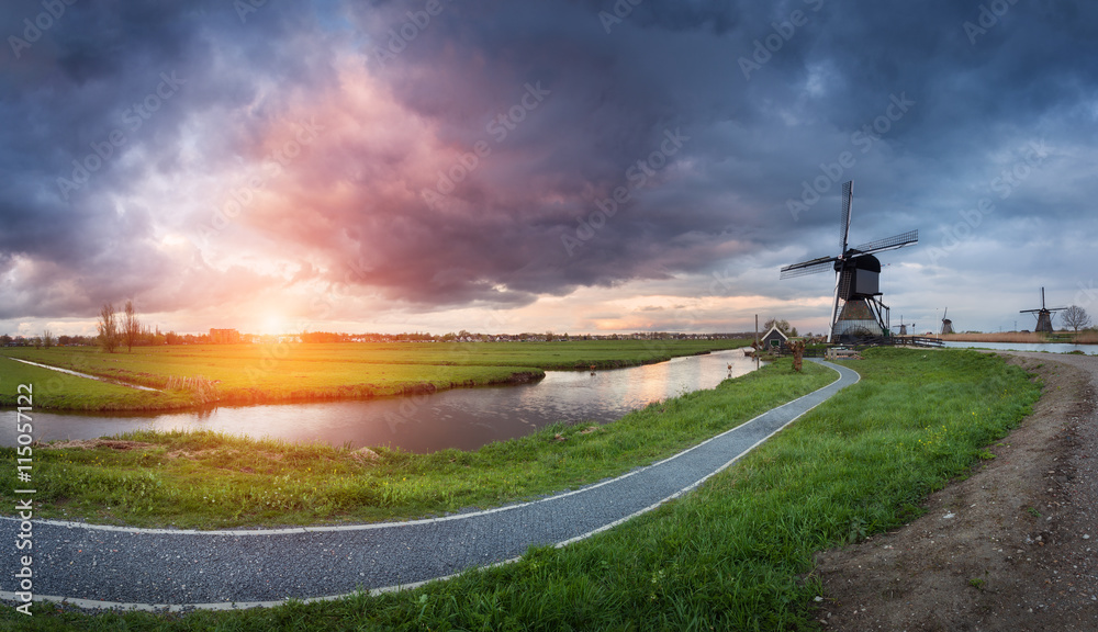 荷兰传统风车和运河附近的小路景观。五颜六色的日落下的云朵