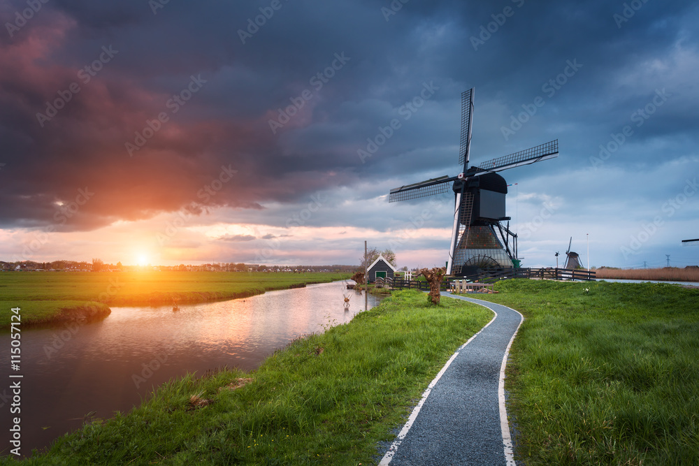 荷兰传统风车和运河附近的小路景观。五颜六色的日落下的云朵