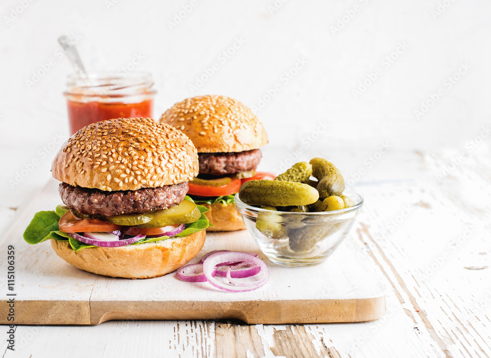 两个新鲜的自制汉堡、泡菜、番茄酱和洋葱圈放在白色木制服务板上