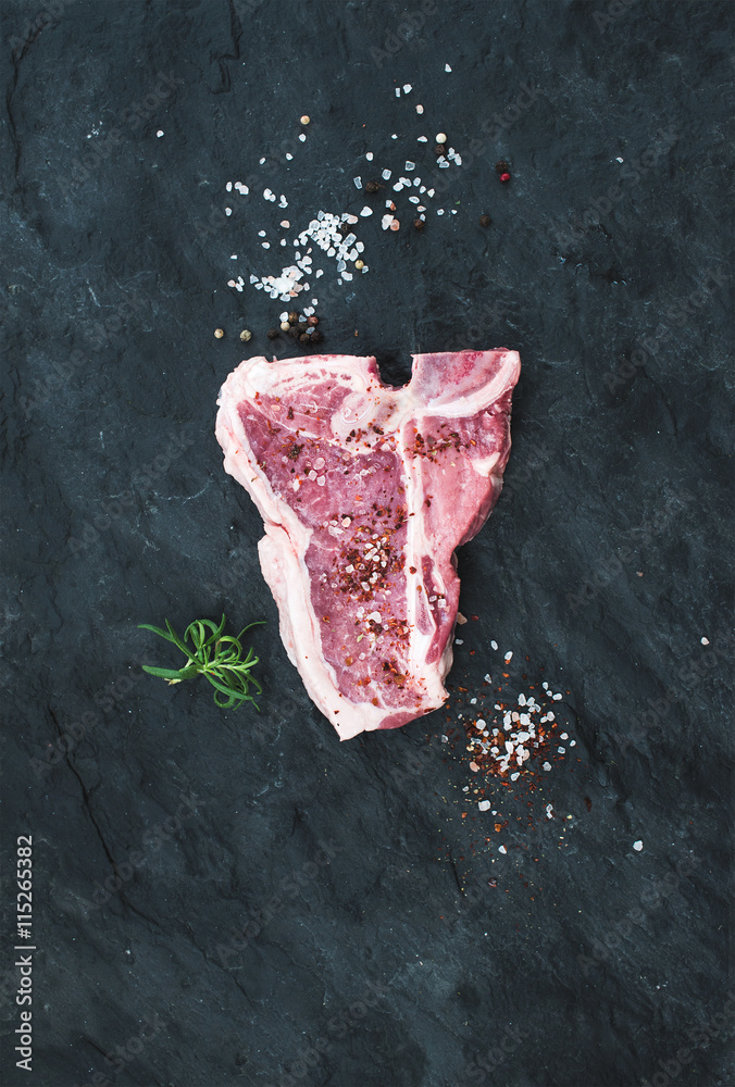 Raw fresh t-bone beef steak with salt, spices and rosemary over black slate stone background, copy s