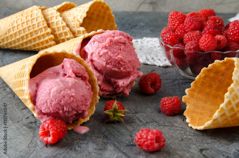 Raspberry ice cream with ice cream cones on stone table.