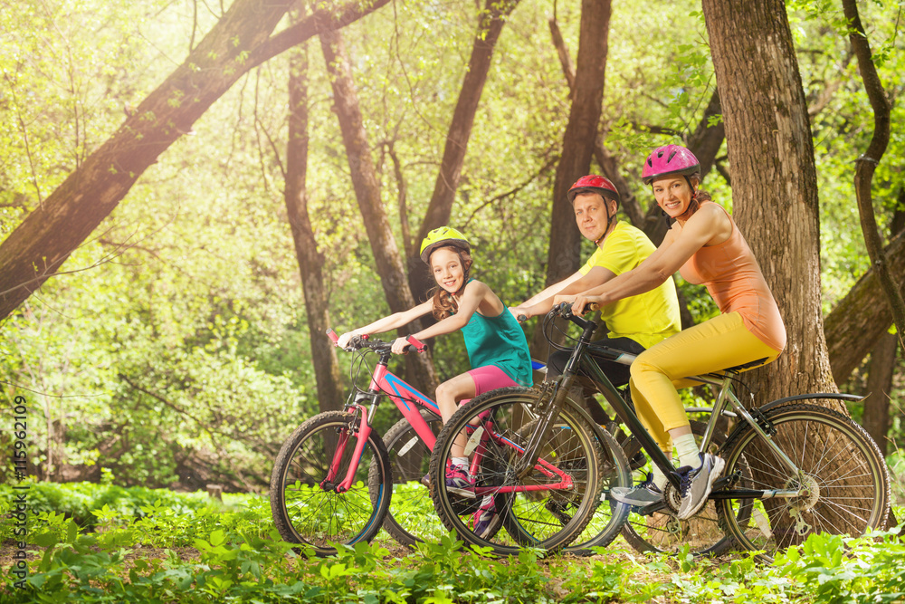阳光明媚的森林里，一家人骑着自行车积极微笑
