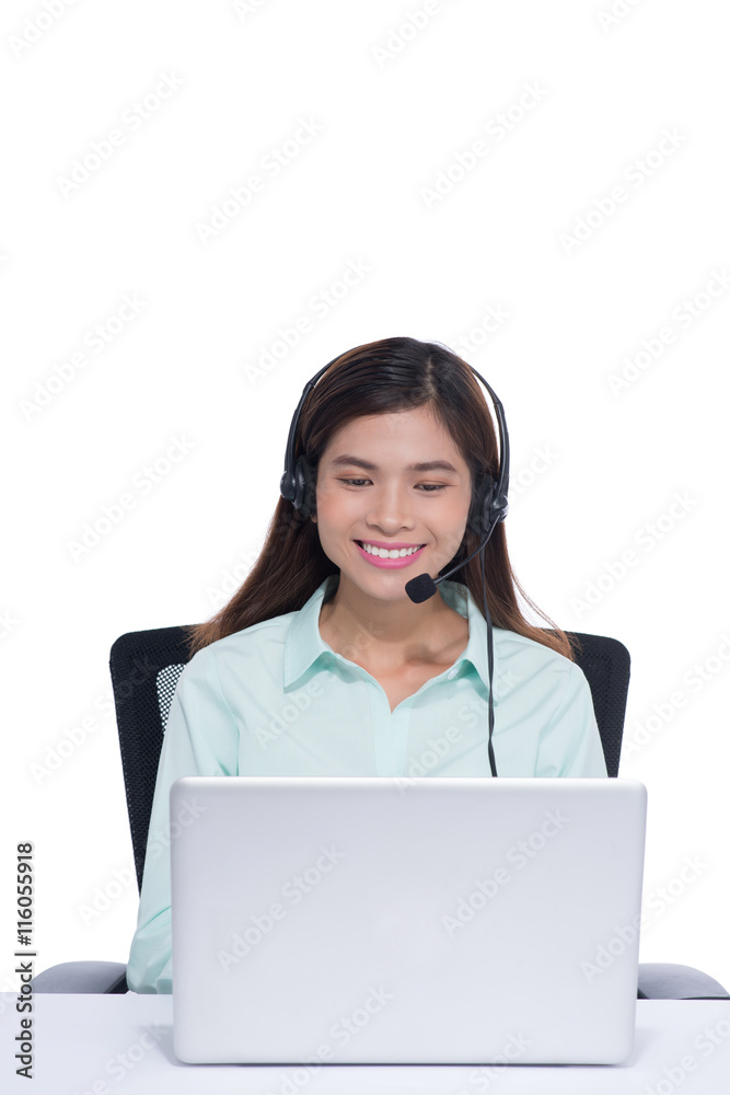 快乐的亚洲年轻女性在办公室里用耳机坐着用笔记本电脑工作