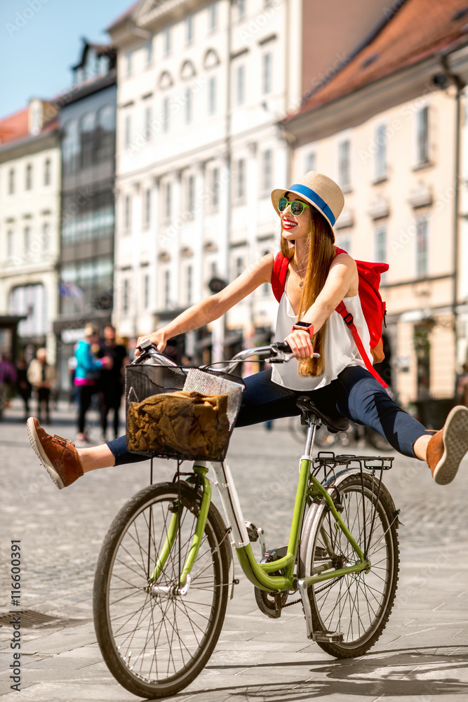 Young female tourist with backpack and hat having fun riding a bicycle in the old city center of Lju