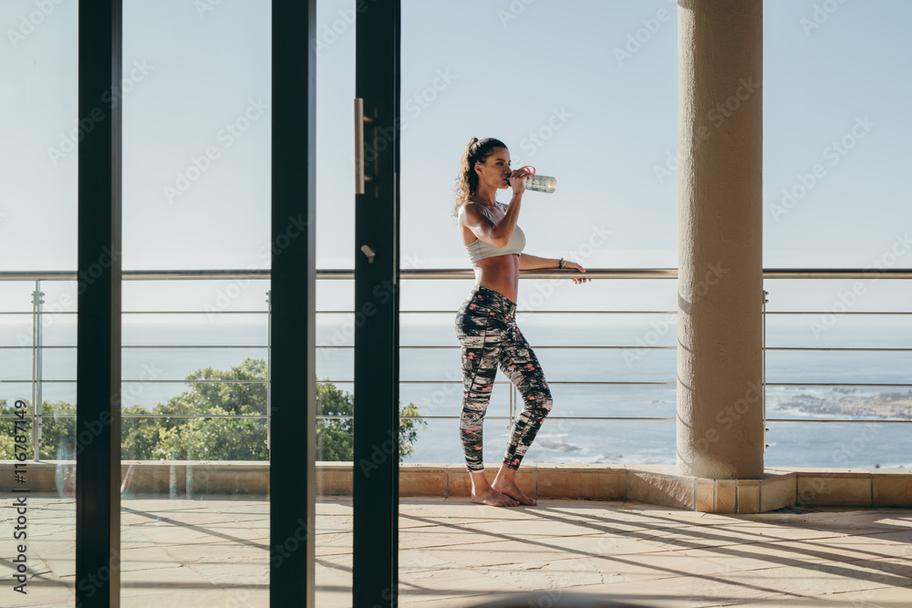 健身女士站在阳台上喝水