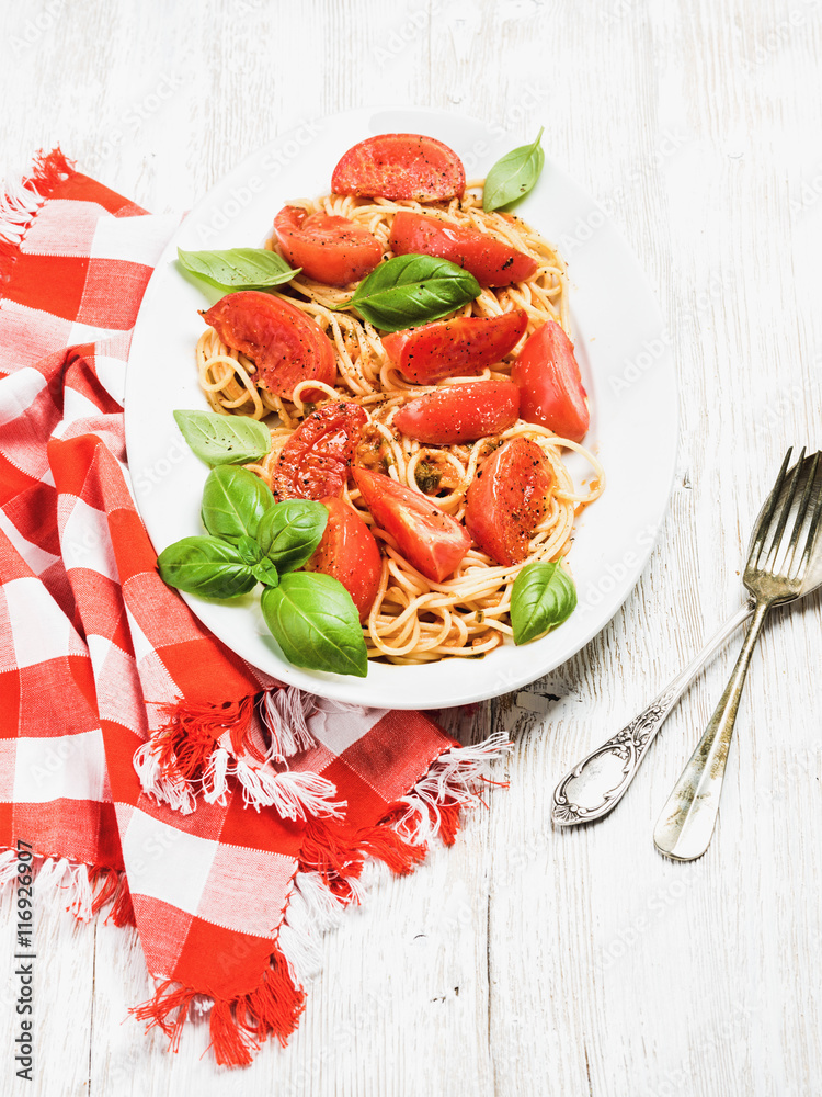 意大利面晚餐。意大利面配烤番茄和新鲜罗勒，放在白色木制背景面包上的椭圆形盘子里