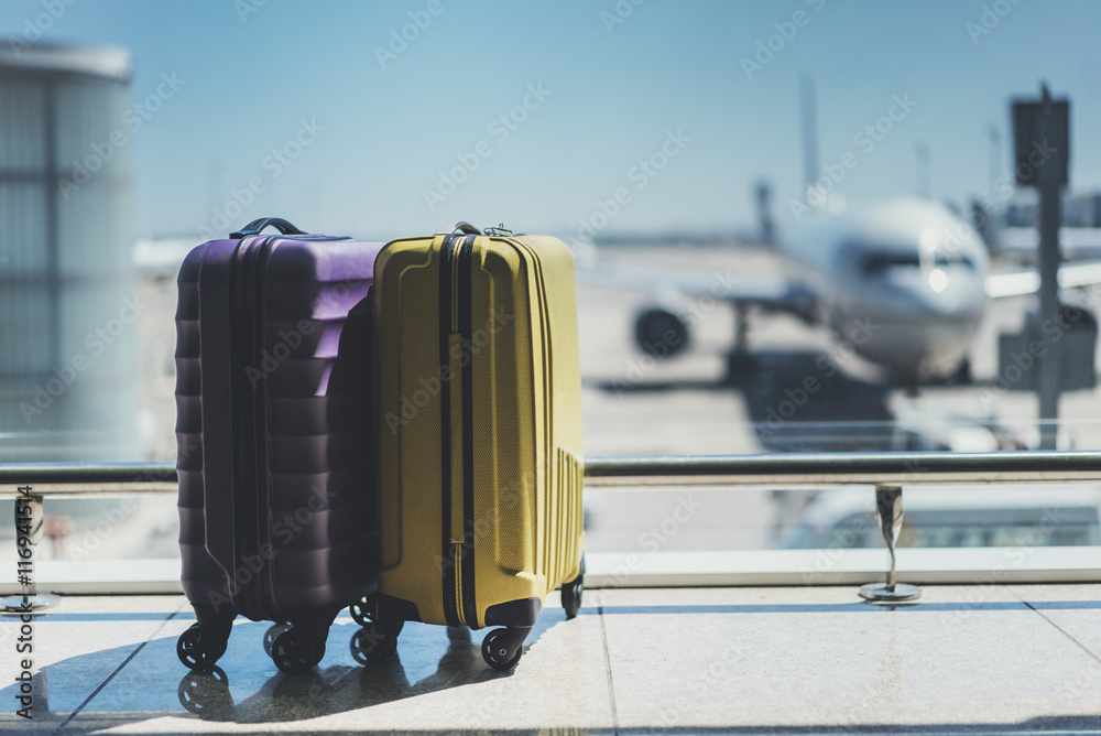 Two suitcases in the airport departure lounge, airplane in the blurred background, summer vacation c