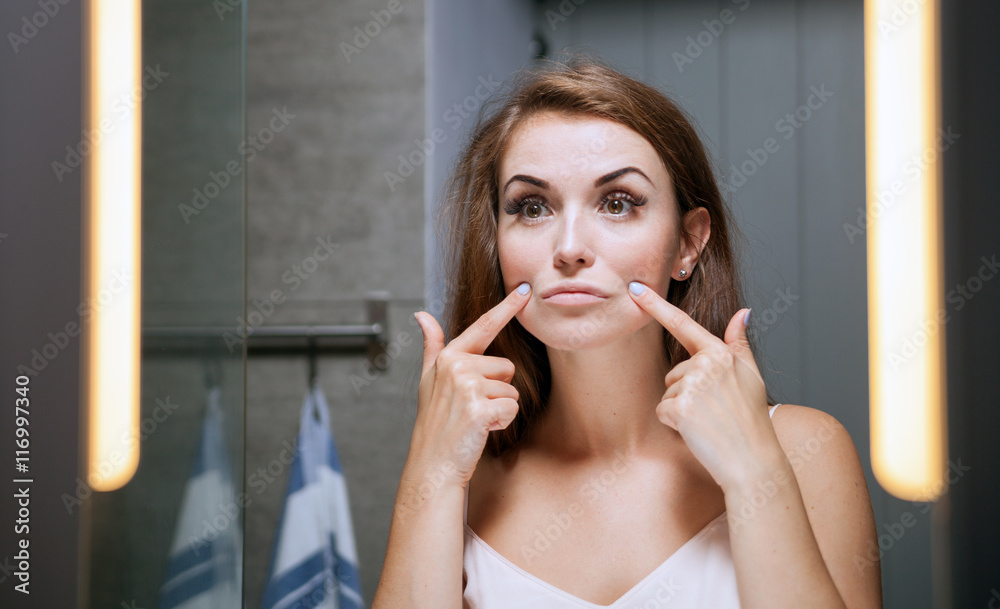 女人在浴室镜子前检查脸上的皱纹
