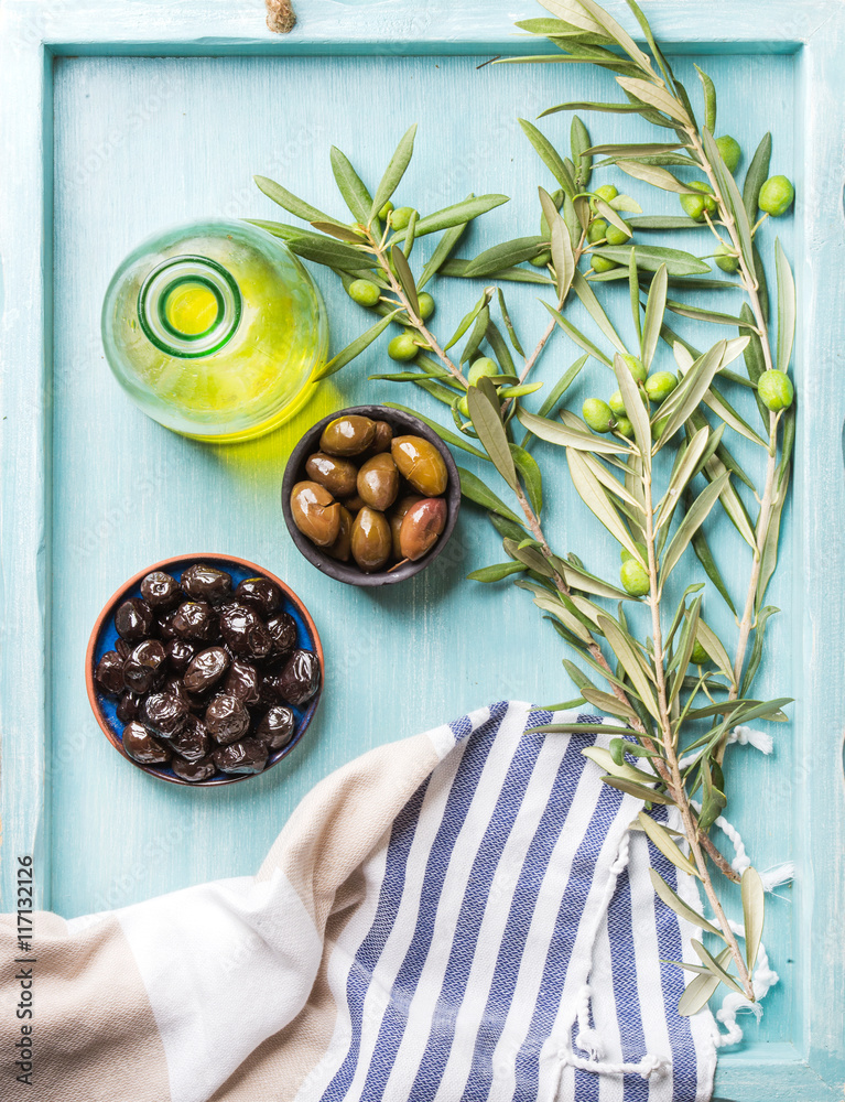 两个碗，里面有腌制的青橄榄和黑橄榄，橄榄枝和一瓶蓝色草皮上的橄榄油