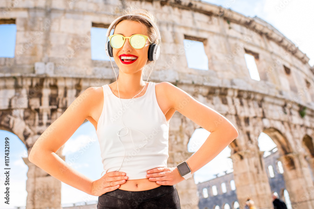 普尔古老圆形剧场附近一位戴着耳机和太阳镜的年轻运动女性的肖像