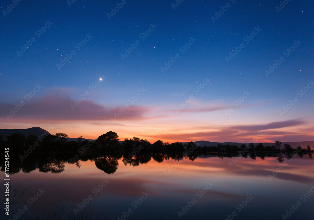Beautiful night landscape on the mountain lake with stars and reflected clouds in water in spring. C