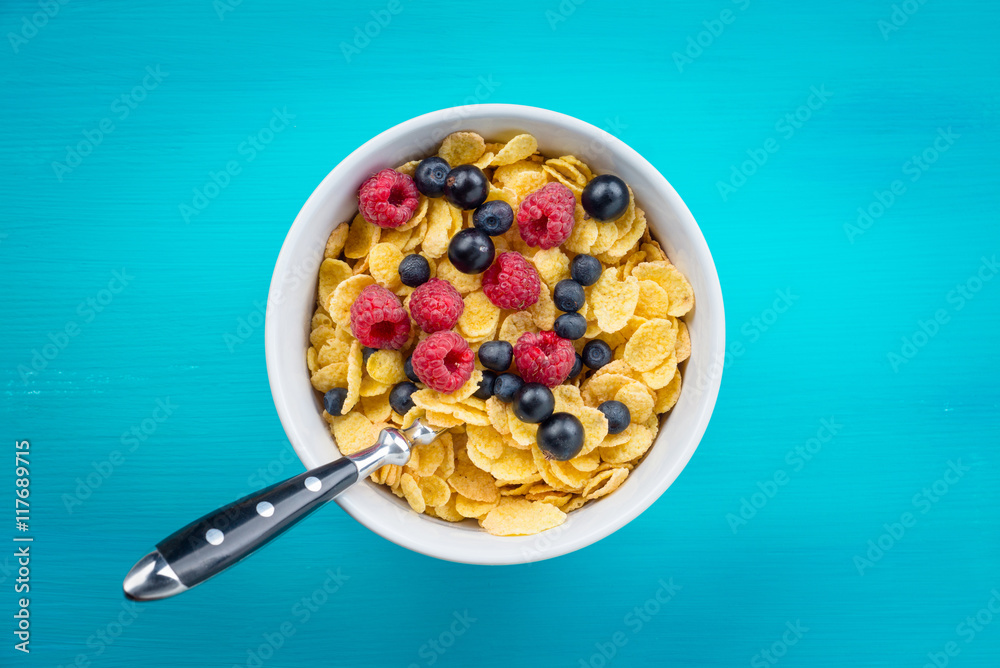 Cornflakes cereal with raspberries and bilberries and black currant in a white bowl on the blue wood