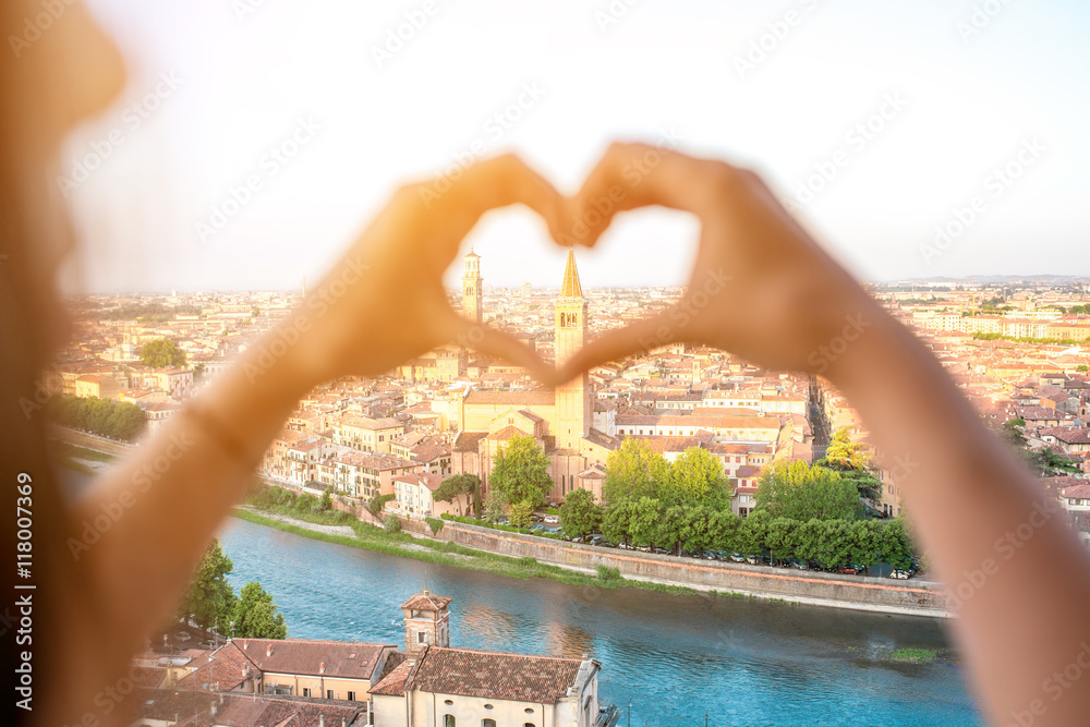 维罗纳城市景观背景下的女性双手塑造心形。维罗纳是世界上著名的爱情之城