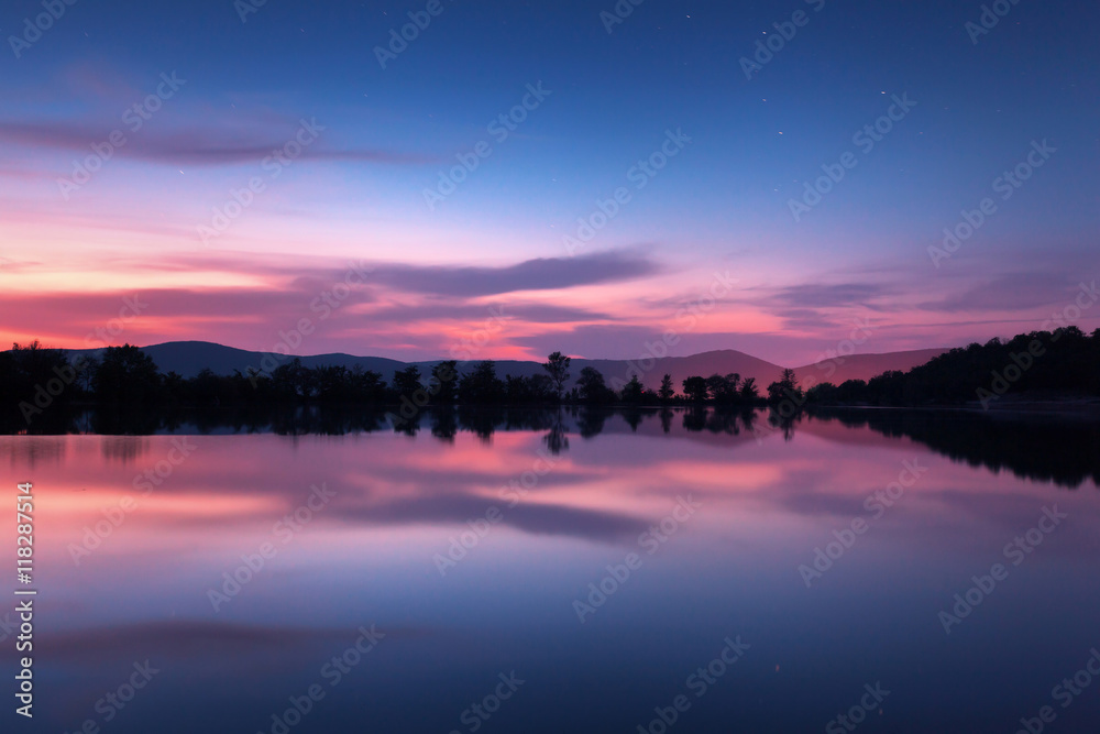 Beautiful night landscape on the mountain lake with stars and reflected clouds in water in spring.Co