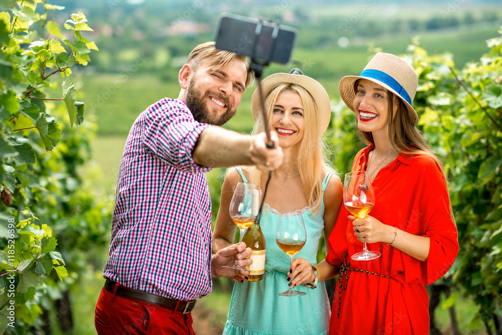 Three friends with hats and wine glasses having fun making selfie photo with smartphone and selfie s