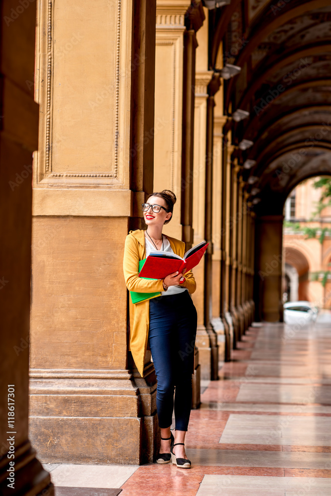 年轻的女学生穿着休闲，拿着书站在博洛尼亚著名的拱形画廊里